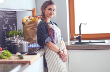 Mutfakta sobanın yanında duran genç bir kadın. .