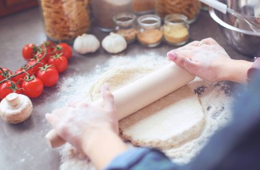 Güzel bir kadın mutfakta pasta pişiriyor. Masanın yanında duruyor..