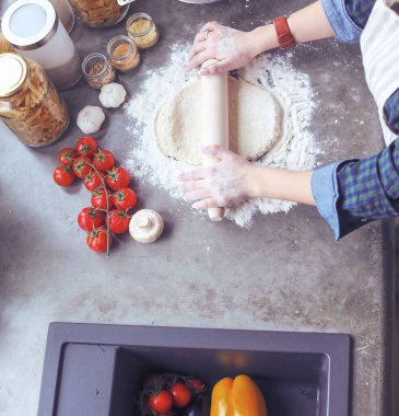 Güzel bir kadın mutfakta pasta pişiriyor. Masanın yanında duruyor..