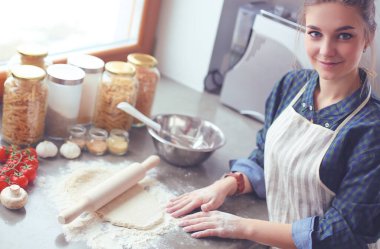 Güzel bir kadın mutfakta pasta pişiriyor. Masanın yanında duruyor..