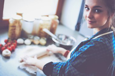 Güzel bir kadın mutfakta pasta pişiriyor. Masanın yanında duruyor..