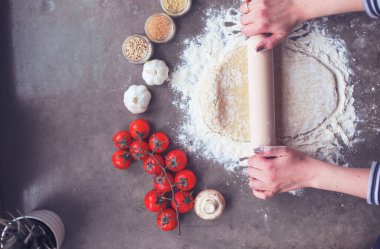 Güzel bir kadın mutfakta pasta pişiriyor. Masanın yanında duruyor.