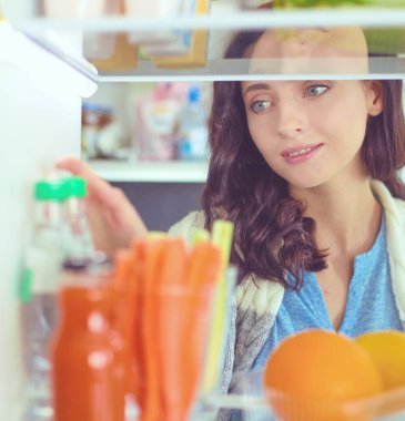 Sağlıklı yiyecek, sebze ve meyvelerle dolu açık buzdolabının yanında duran kadın portresi. Kadın portresi