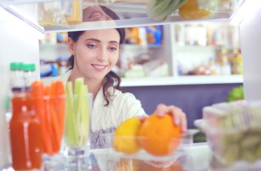 Sağlıklı yiyecek, sebze ve meyvelerle dolu açık buzdolabının yanında duran kadın portresi. Kadın portresi
