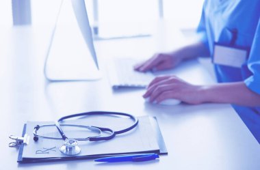 Kadın doktor masada oturuyor ve hastanede dizüstü bilgisayarla çalışıyor.