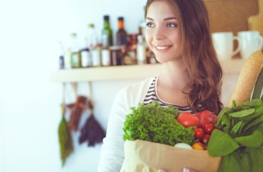 Elinde sebzeli alışveriş torbası tutan genç bir kadın.