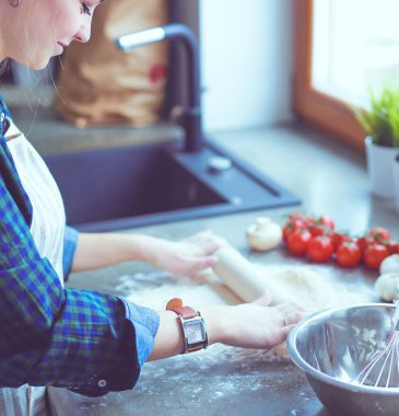 Güzel bir kadın mutfakta pasta pişiriyor. Masanın yanında duruyor..