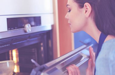 Güzel genç bayan pastasının fırında ne yaptığını kontrol ediyor.