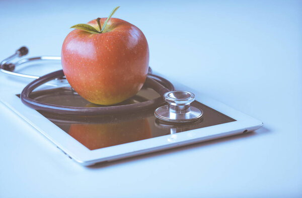 Medical stethoscope and red apple lying on a tablet isolated on white background.