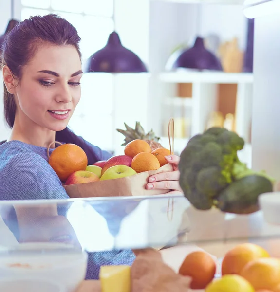 Smiling woman taking a fresh fruit out of the fridge, healthy food concept — Stock Photo, Image
