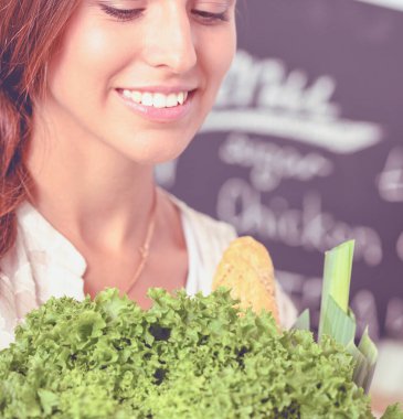 Mutfakta elinde sebzelerle gülümseyen genç bir kadın. Gülümseyen genç kadın