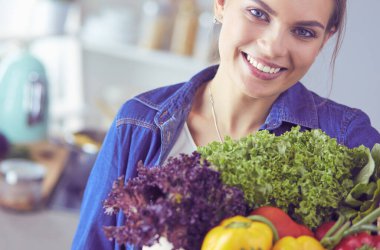 Sebzeli alışveriş poşeti taşıyan genç bir kadın. Mutfakta duruyor.