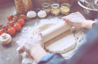 Güzel bir kadın mutfakta pasta pişiriyor. Masanın yanında duruyor.