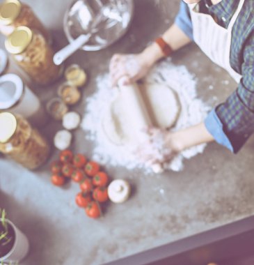 Güzel bir kadın mutfakta pasta pişiriyor. Masanın yanında duruyor.