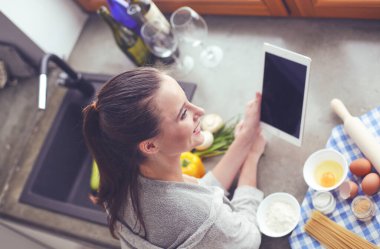 Güzel bir kadın mutfakta pasta pişiriyor. Masanın yanında duruyor..