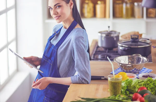 Ung kvinna använder en surfplatta dator för att laga mat i sitt kök — Stockfoto