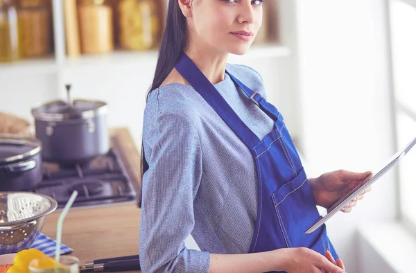 Jovem usando um computador tablet para cozinhar em sua cozinha — Fotografia de Stock