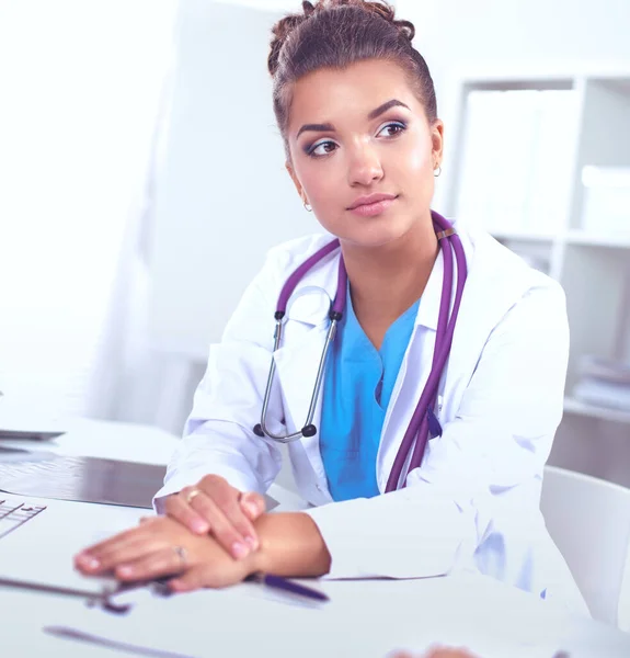 Hermosa joven sonriente doctora sentada en el escritorio y escribiendo. —  Fotos de Stock