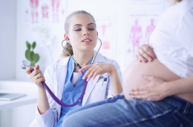 Steteskoplu genç bayan doktor hastanede hamile bir kadınla konuşuyor..