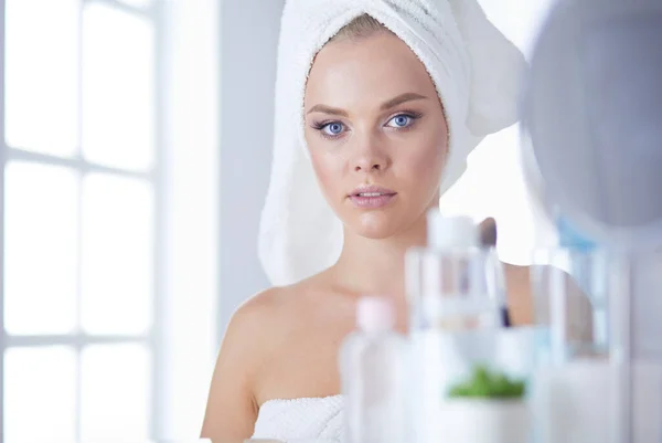 Молодая женщина в халате смотрит в зеркало ванной комнаты — стоковое фото