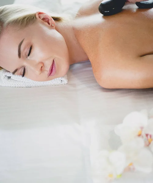 Mujer joven en el salón de spa, recibiendo piedras masaje — Foto de Stock