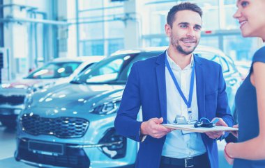 Araba satıcısı araba galerisindeki mutlu müşteriye araba satar ve anahtarları teslim eder.