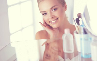 Bornozlu genç kadın banyo aynasına bakıyor.