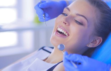 Dişçi muayenehanesinde diş muayenesi yapan ağzı açık genç bir kadın hasta..