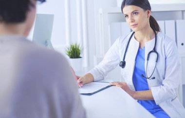 Doktor ve hasta hastane danışma odasında tıbbi sorunları tartışıyorlar. Doktor hasta formunu dolduruyor.