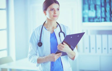 Steteskoplu gülümseyen genç bayan doktor hastane danışma odasında bir dosya tutuyor.