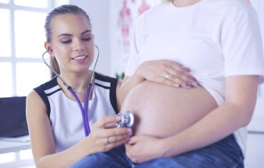 Genç bayan doktor klinikte hamile kadını muayene ediyor..