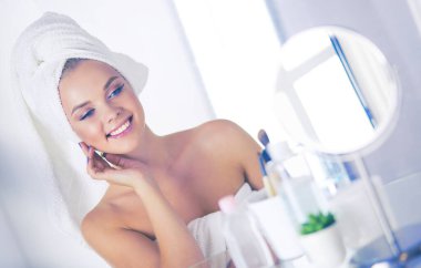 Bornozlu genç kadın banyo aynasına bakıyor.