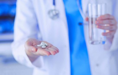 Doktorların ellerinde haplar ve bir bardak su tutarken yakın plan çekimleri..