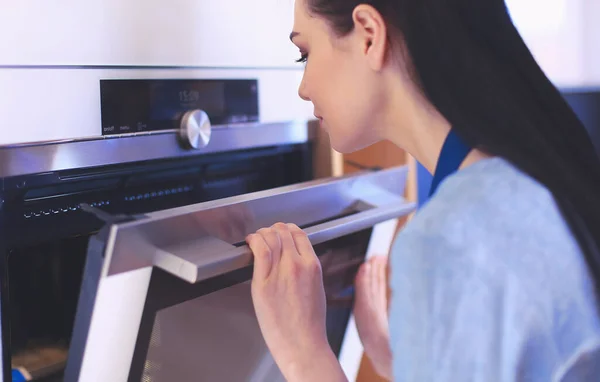 Hermosa joven comprobando cómo le va a su pastel en el horno — Foto de Stock