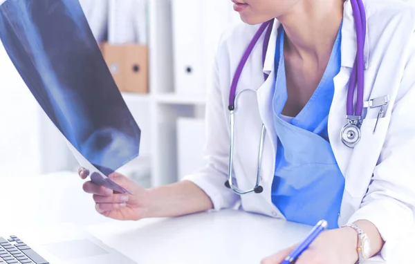 Doctora joven estudiando imagen de rayos X sentada en el escritorio —  Fotos de Stock