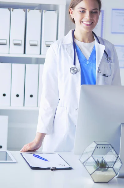 Young doctor woman standing near table, isolated on white background