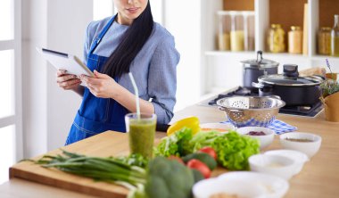 Mutfakta yemek yapmak için tablet bilgisayar kullanan genç bir kadın.