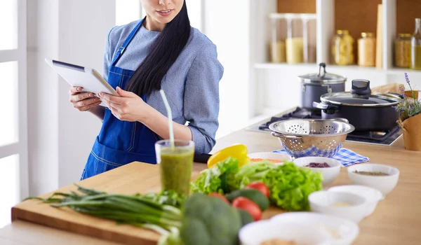 Mutfakta yemek yapmak için tablet bilgisayar kullanan genç bir kadın.