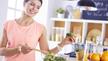 Gülümseyen genç kadın mutfakta taze salata karıştırıyor..