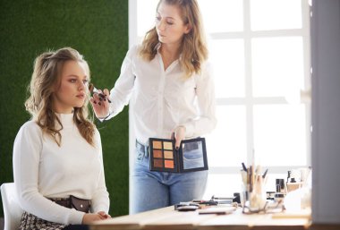 Makyöz, genç bir kadının profesyonel makyajını yapıyor.