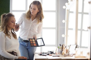 Makyöz, genç bir kadının profesyonel makyajını yapıyor.