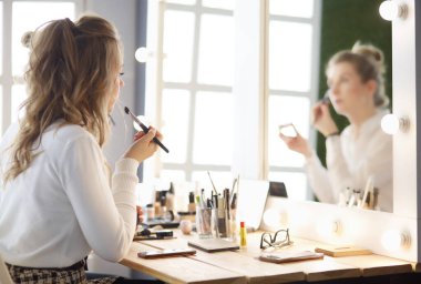 Makyaj sanatçısı, mankenlerin gözüne beyaz göz farı sürüyor ve arka planda göz farı olan bir kabuk tutuyor.