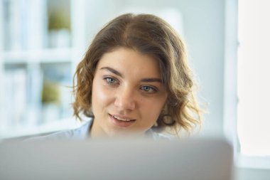 Mutlu güzel kadın rahat koltukta dizüstü bilgisayar kullanıyor.