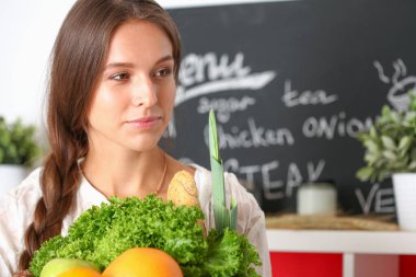 Mutfakta elinde sebzelerle gülümseyen genç bir kadın. Gülümseyen genç kadın