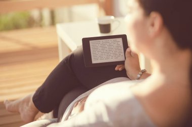 Touchpad ile kanepede oturan gülümseyen genç kadın.