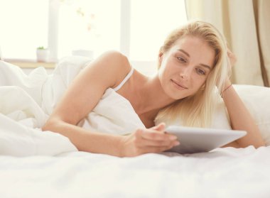 Elinde boş ekranlı dijital tablet tutan ve yatak odasında kameraya gülümseyen bir kız.