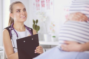 Steteskoplu ve tabletli genç kadın doktor hastanede hamile bir kadınla konuşuyor..