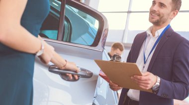 Kadın satıcısı galeride yeni bir arabanın yanında duruyor.