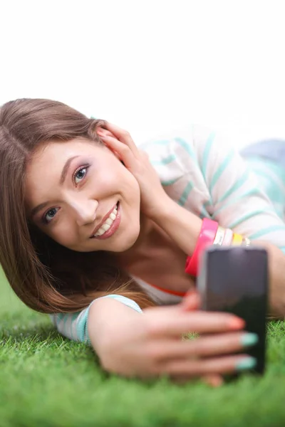 Güzel genç bir kadın yeşil çimenlerde yatarken telefonuyla selfie çekiyor. Güzel genç bir kadın selfie çekiyor. — Stok fotoğraf