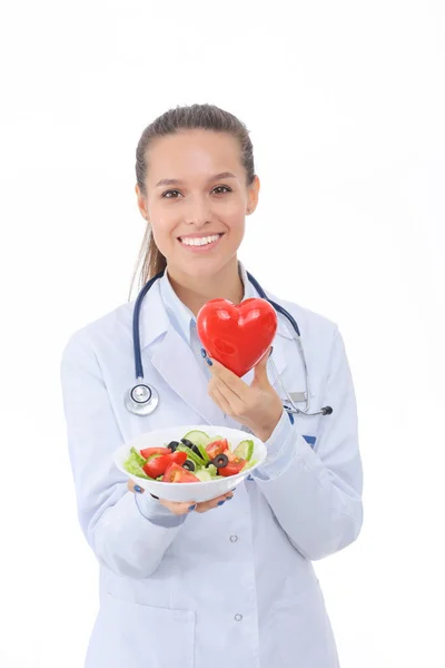 Portrait of a beautiful woman doctor holding a plate with fresh vegetables and red heart. Woman doctors. — Stock Photo, Image